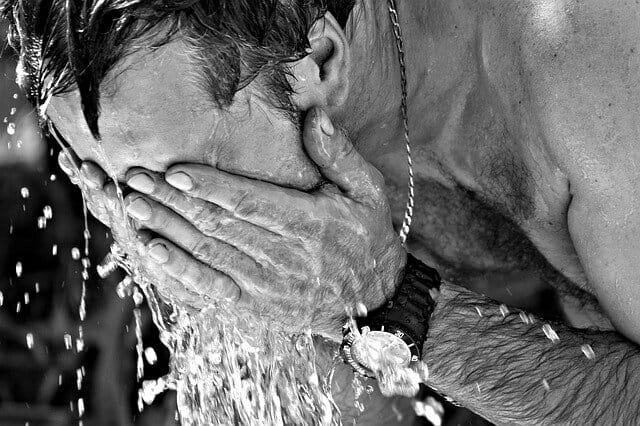 άνδρας ιδρωμένος ρίχνει νερό στο πρόσωπό του για να δροσιστεί