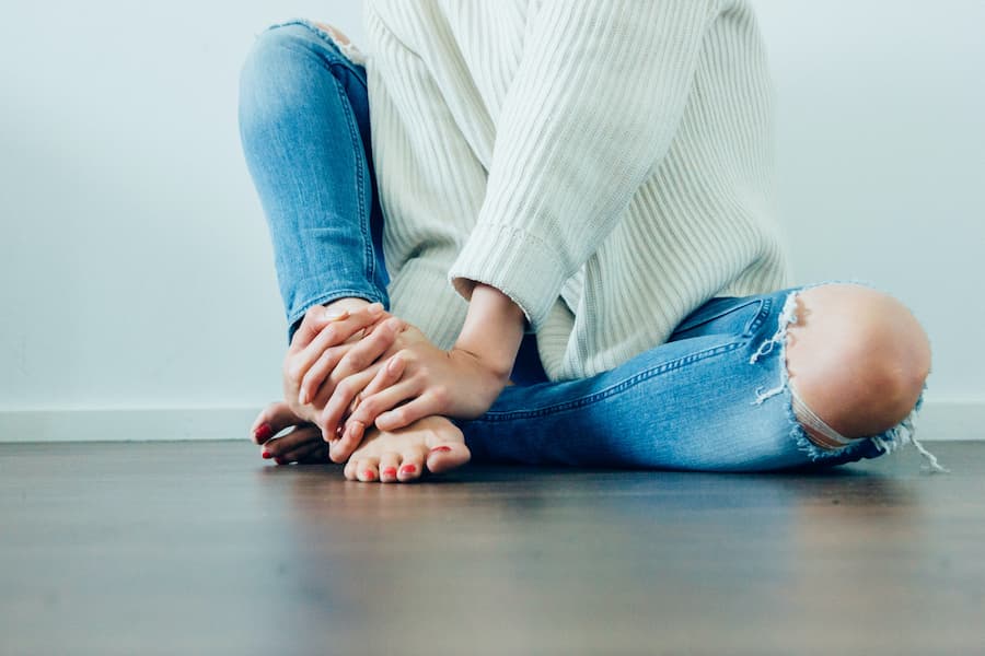 κοπέλα που φορά τζιν και πουλόβερ είναι καθισμένη στο πάτωμα και με τα δύο της χέρια πιάνει το ένα της πόδι
