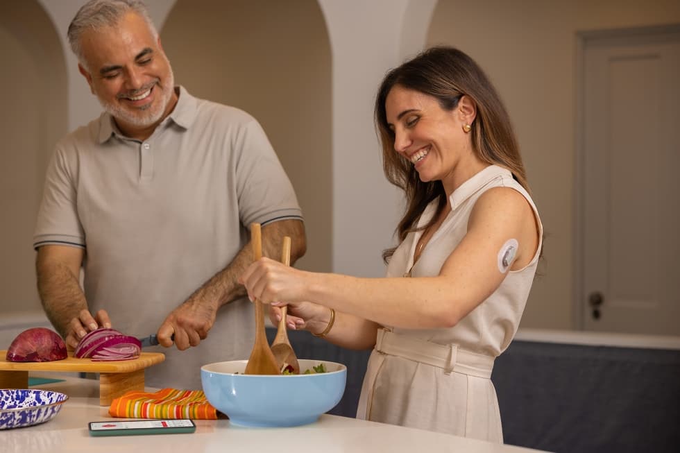 γυναίκα ανακατεύει σαλάτα ενώ χαμογελά μαζί με έναν άντρα που στέκεται δίπλα της